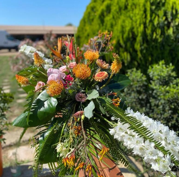 Arranjament floral amb flors de temporada en tons taronja, rosats i blancs, amb fullatge verd, per a la decoració d’un casament a l’exterior.
