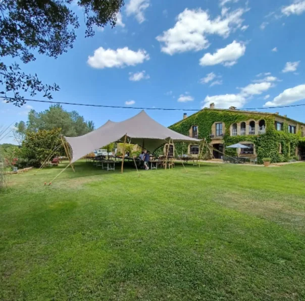 Masia a la Costa Brava amb una carpa instal·lada i un extens camp verd al voltant, creant un espai acollidor i versàtil per a casaments i esdeveniments.