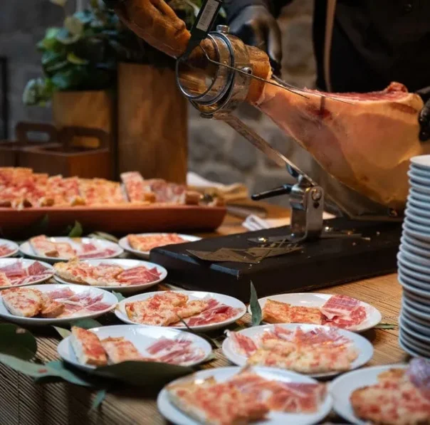 Estació de showcooking amb pernil tallat al moment durant l’aperitiu d’un casament, servit en plats individuals per als convidats.