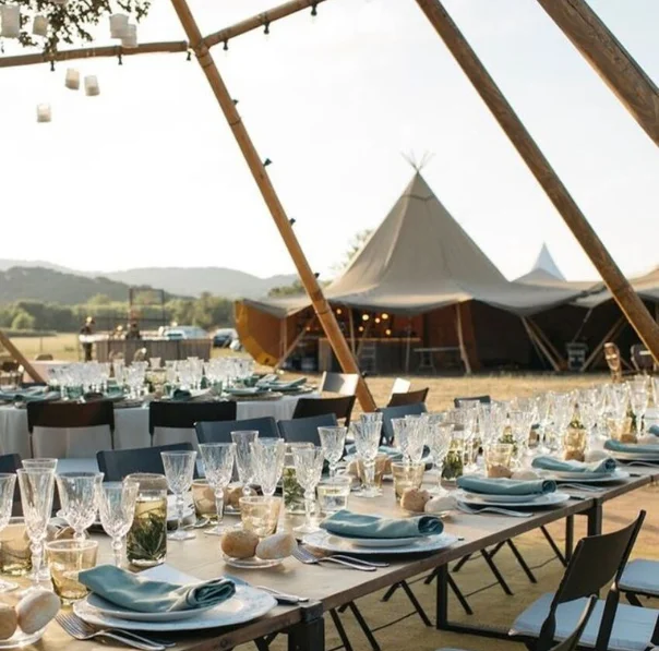 Llarga taula tipus banquet decorada amb elegància davant d’un tipi, creant un espai acollidor i únic per a un casament a Catalunya.