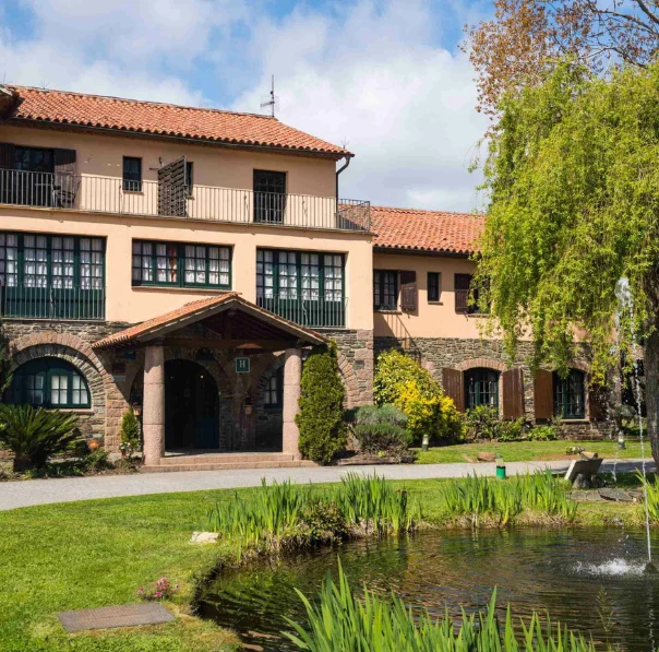 Vista de l’Hotel Sant Bernat amb un petit estany d’aigua en primer pla, envoltat de natura, creant un escenari acollidor i amb encant per a casaments al Montseny.