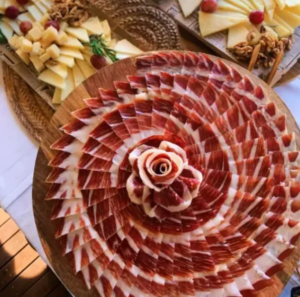 Plat de pernil tallat a mà col·locat amb cura i taula de formatges amb raïm, creant una presentació elegant i gourmet per a un esdeveniment o casament.