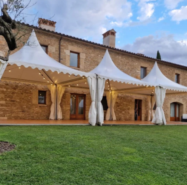 Carpes blanques muntades davant d’una masia de pedra amb jardí, preparades per a la celebració d’un casament a l’aire lliure a l’Empordà.